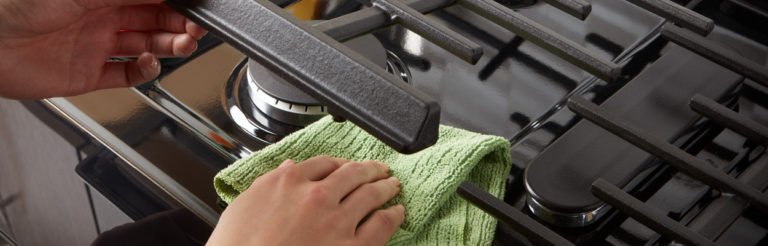 Person wiping stove grate with cloth rag
